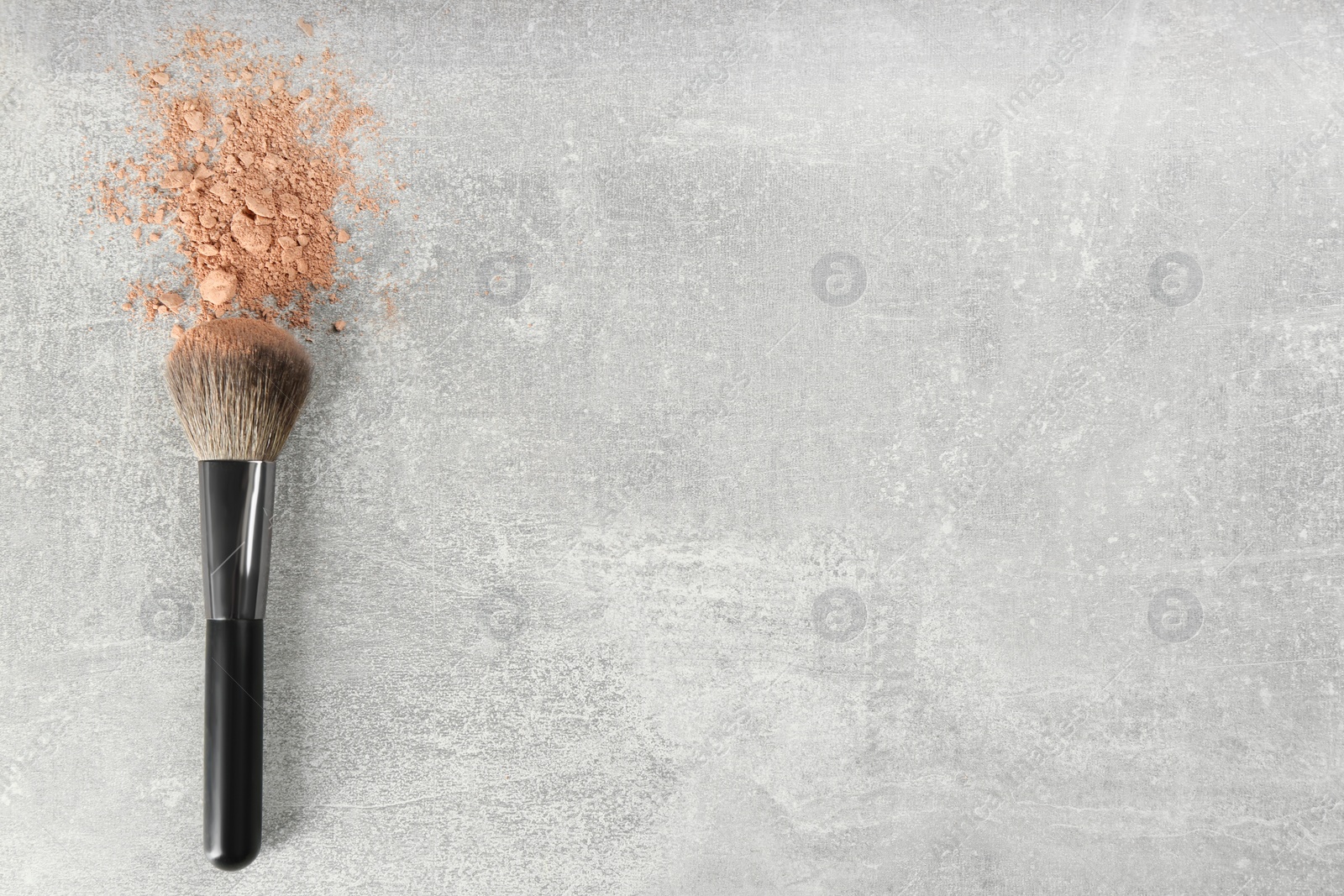 Photo of Makeup brush and scattered face powder on grey stone table, top view. Space for text