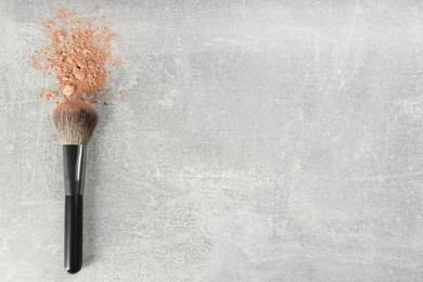 Makeup brush and scattered face powder on grey stone table, top view. Space for text