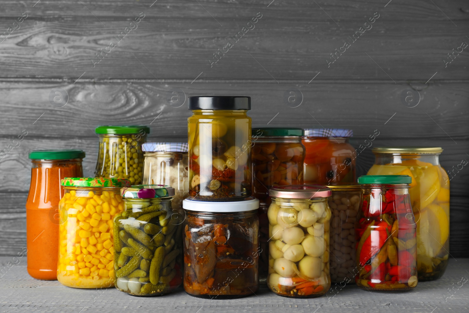 Photo of Jars with pickled vegetables on wooden table against grey background