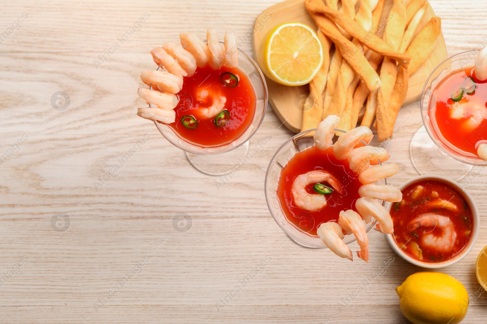 Photo of Tasty shrimp cocktail with sauce in glasses and lemon on light wooden table, flat lay. Space for text