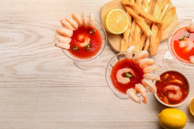 Tasty shrimp cocktail with sauce in glasses and lemon on light wooden table, flat lay. Space for text