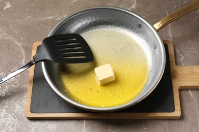 Frying pan with melting butter and spatula on grey table, closeup