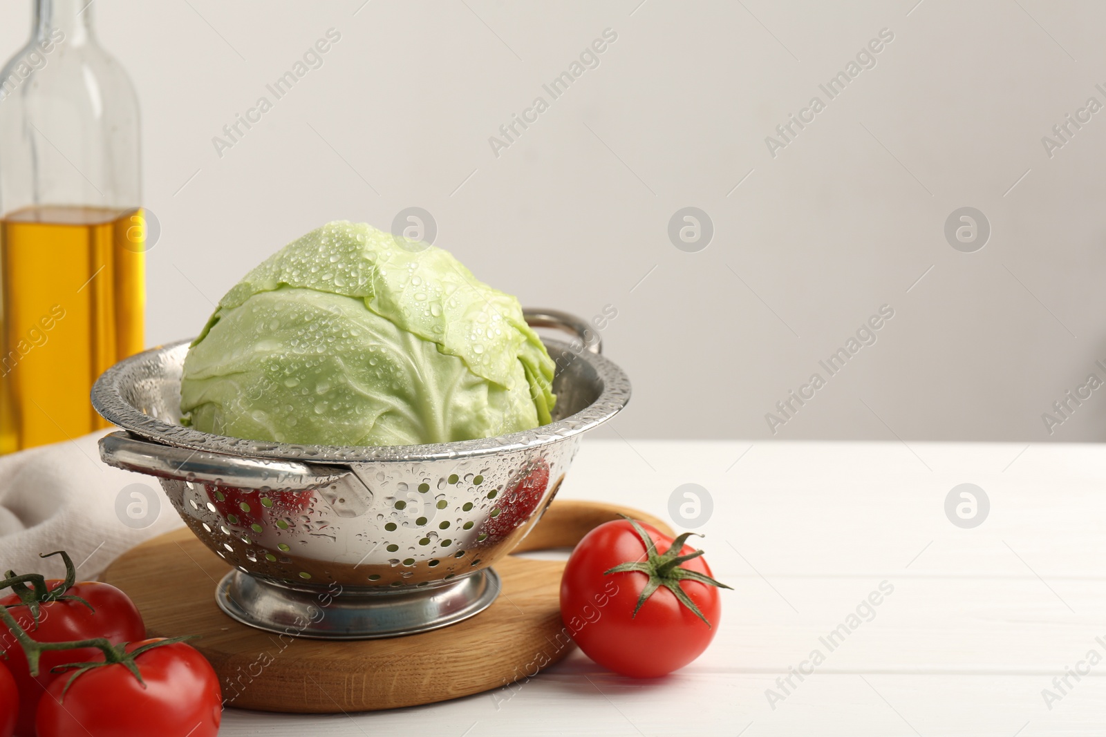 Photo of Wet cabbage in colander and tomatoes on white wooden table, closeup. Space for text