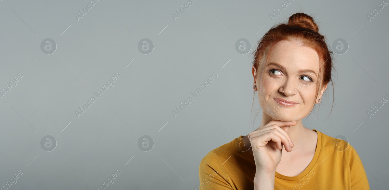 Photo of Portrait of thoughtful red haired woman with charming smile on grey background