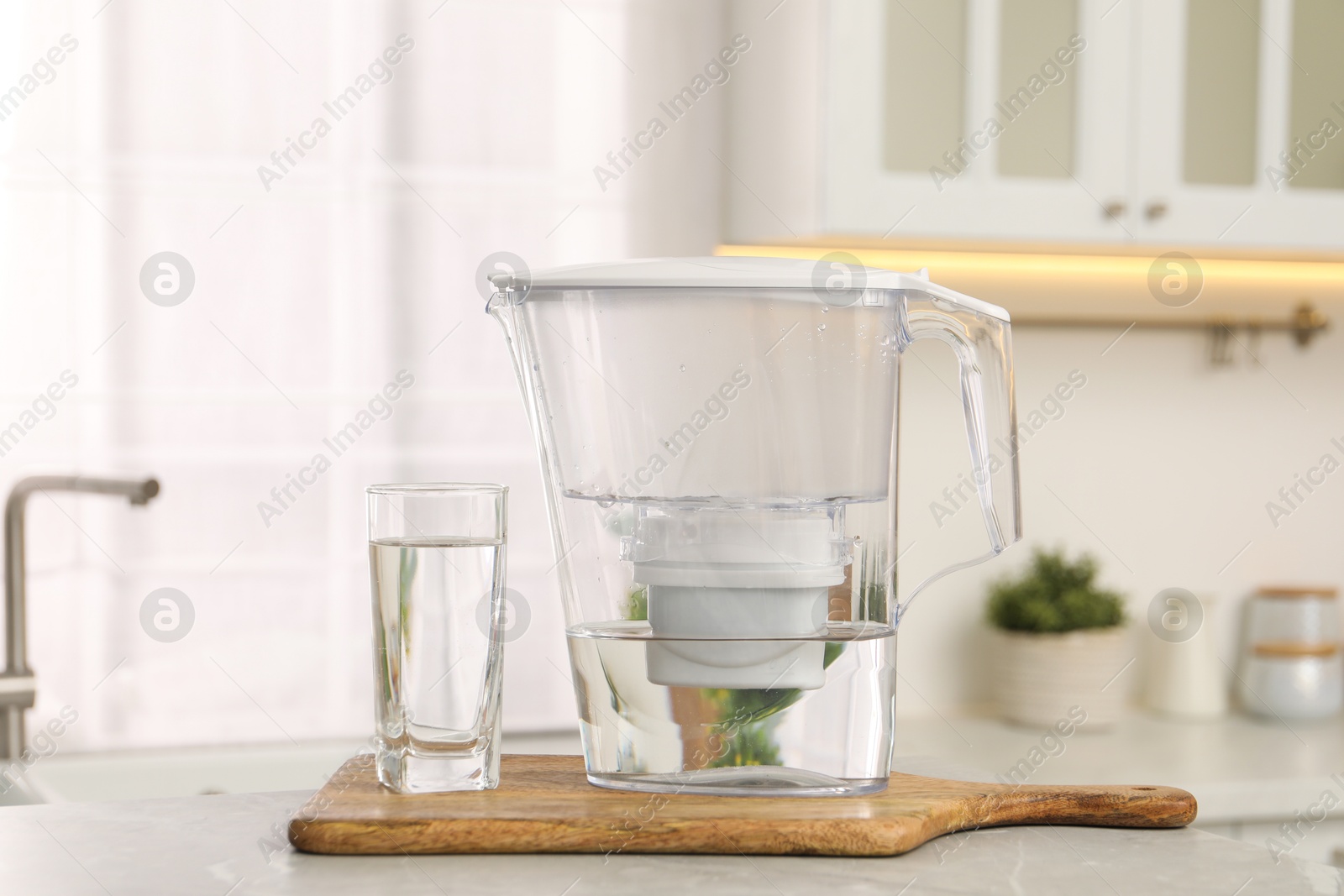 Photo of Water filter jug and glass on light table in kitchen