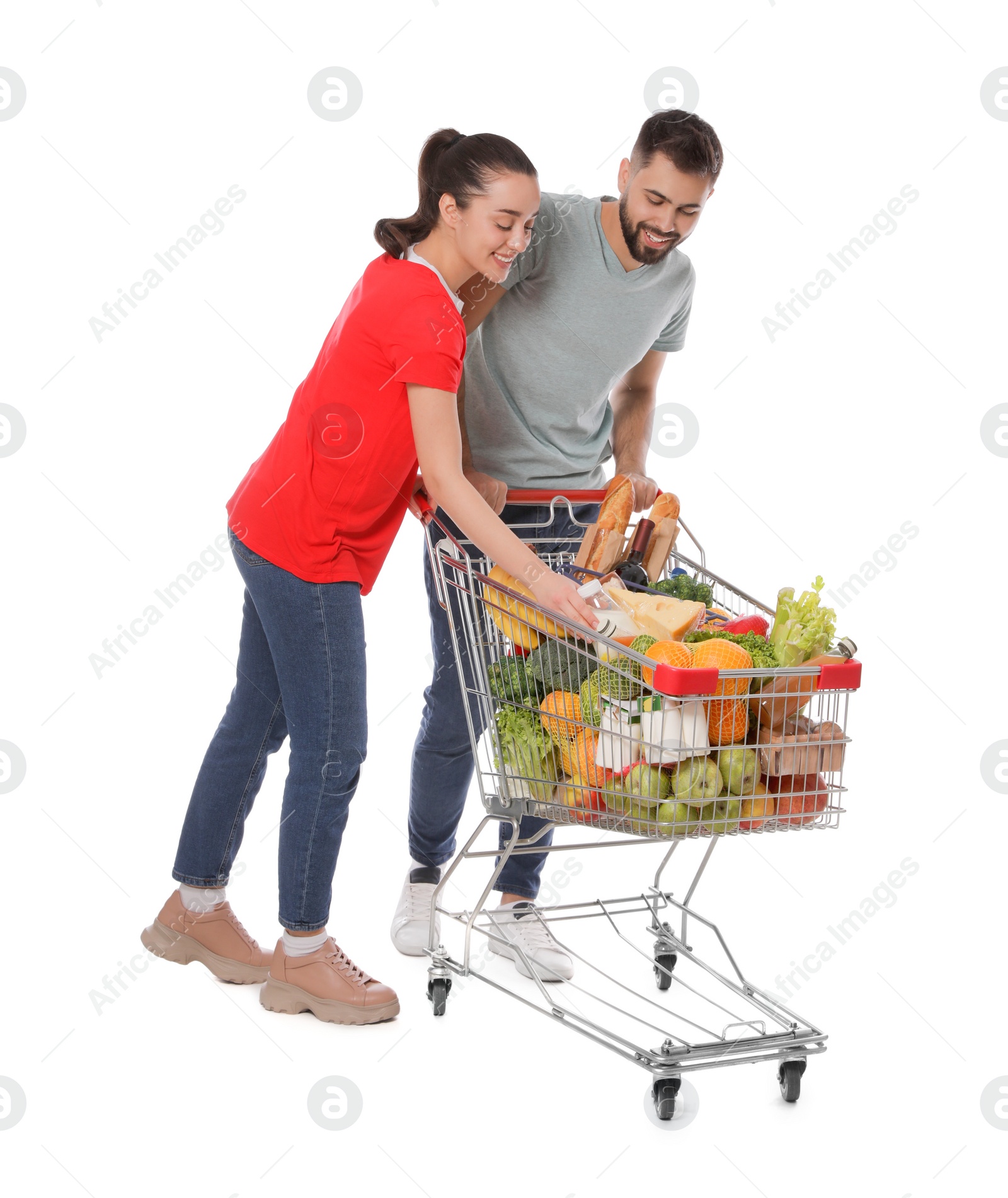 Photo of Happy couple with shopping cart full of groceries on white background