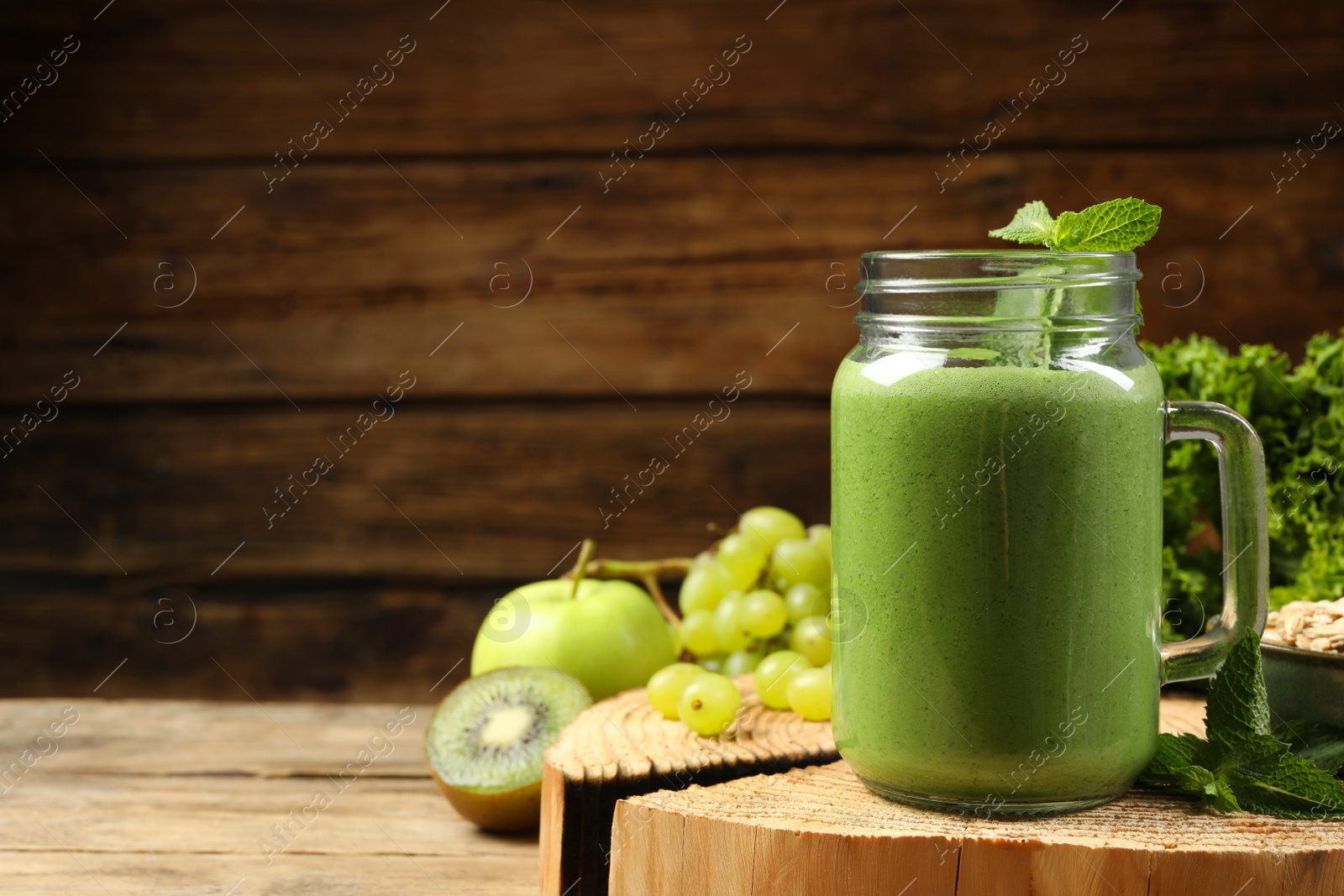 Photo of Mason jar of fresh green smoothie and ingredients on wooden table, space for text