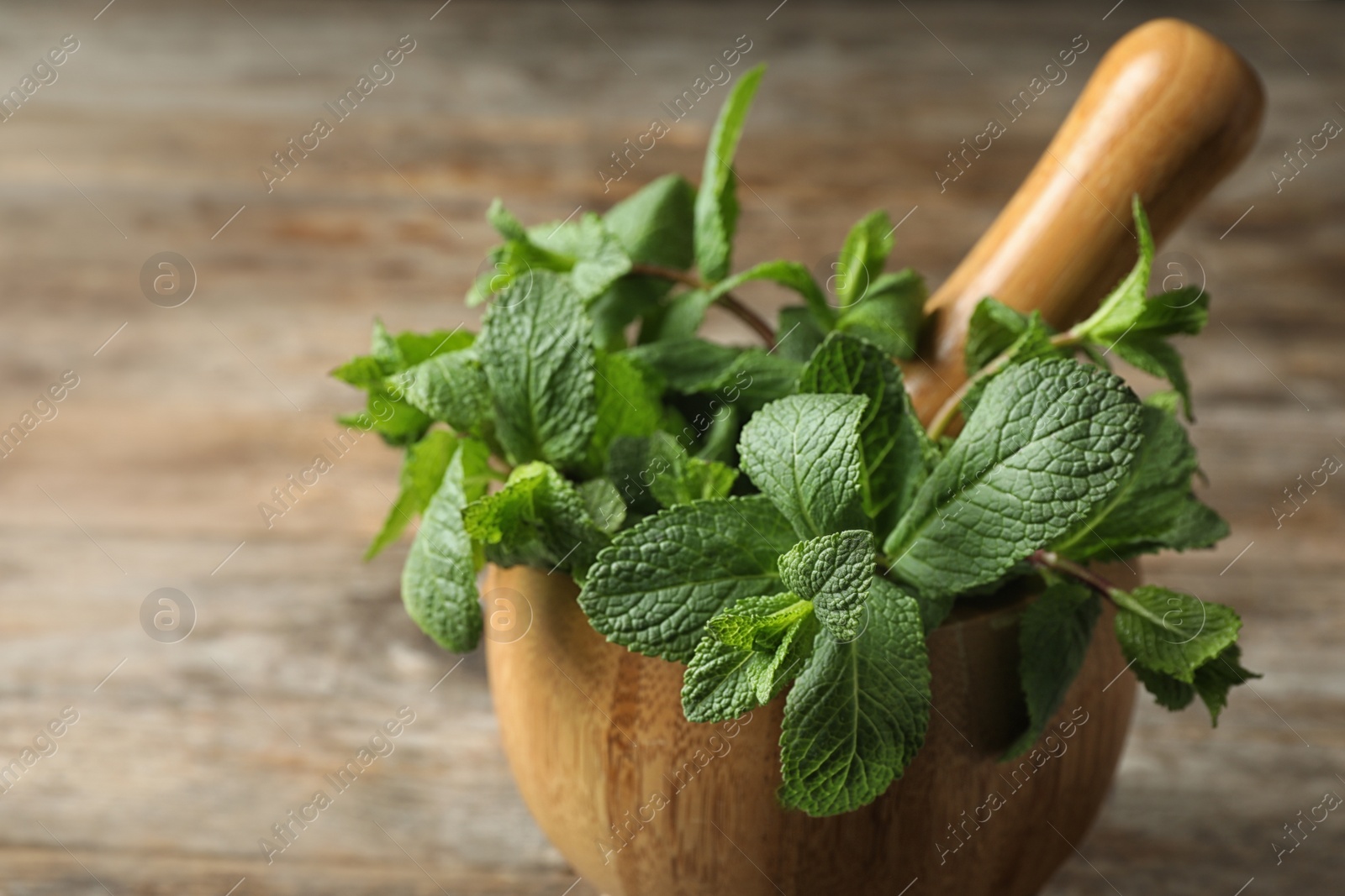 Photo of Wooden mortar with fresh green mint on table, closeup. Space for text