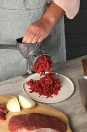 Photo of Woman making beef mince with manual meat grinder at light wooden table, closeup