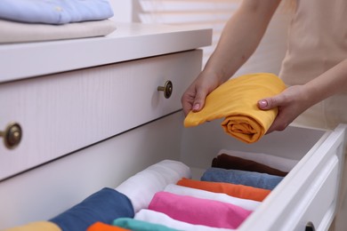 Photo of Woman putting rolled shirt into drawer at home, closeup. Organizing clothes