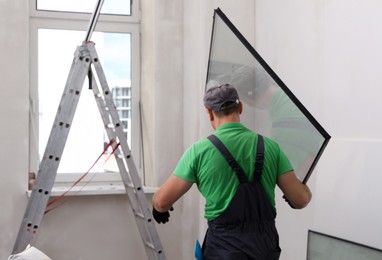 Worker in uniform holding double glazing window indoors, back view