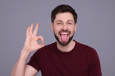 Photo of Happy man showing his tongue and making ok gesture on light grey background