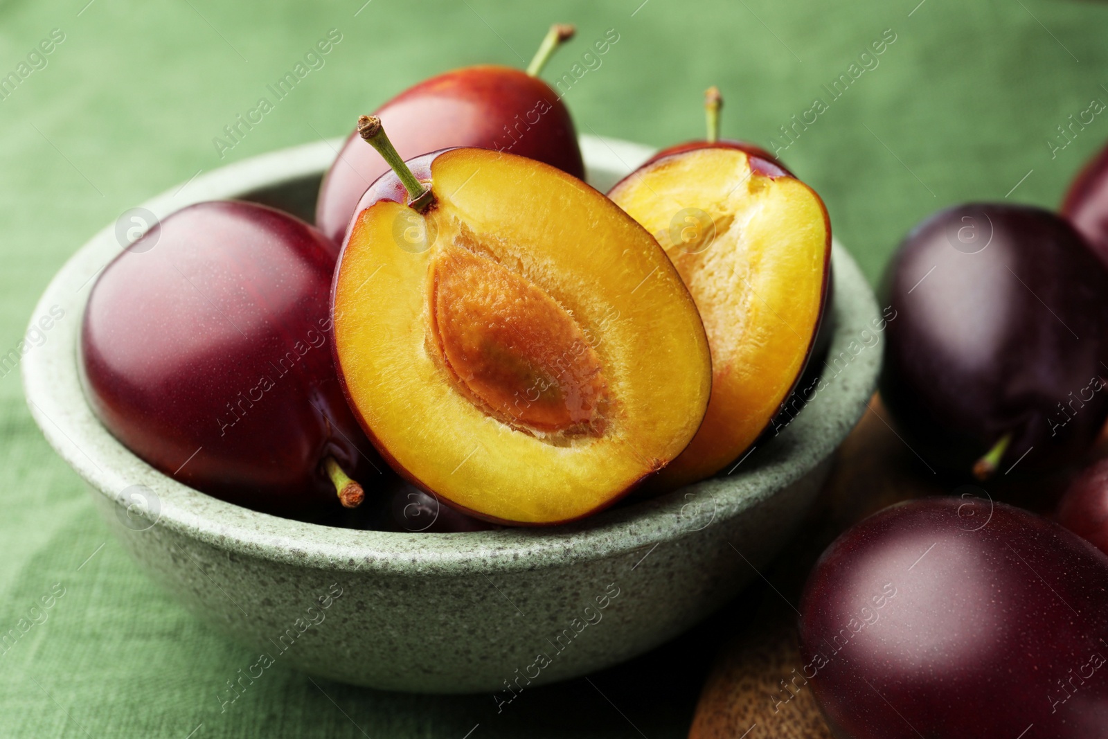 Photo of Many tasty ripe plums on green fabric, closeup