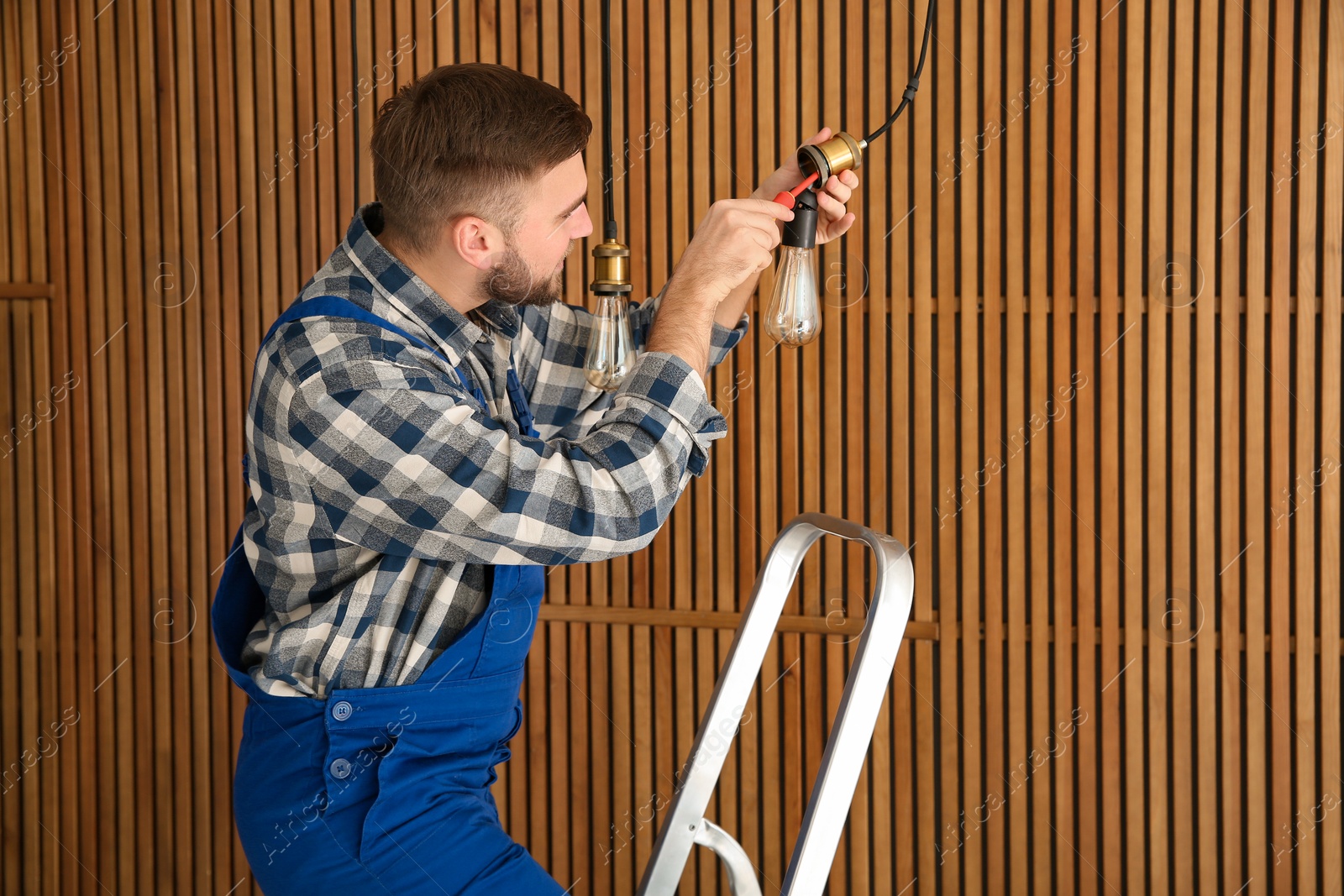 Photo of Electrician with screwdriver repairing ceiling lamp against wooden background. Space for text