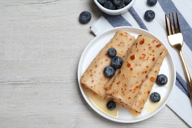 Photo of Delicious crepes with blueberries and honey on white wooden table, flat lay. Space for text