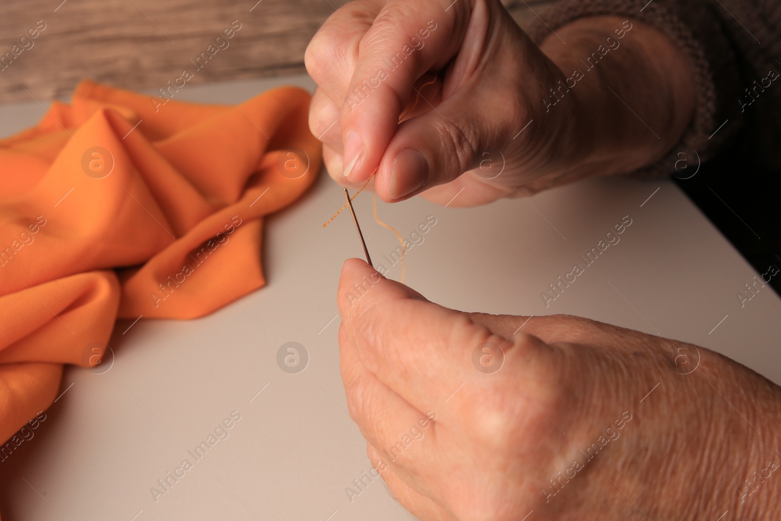 Photo of Closeup view of woman threading needle at beige table