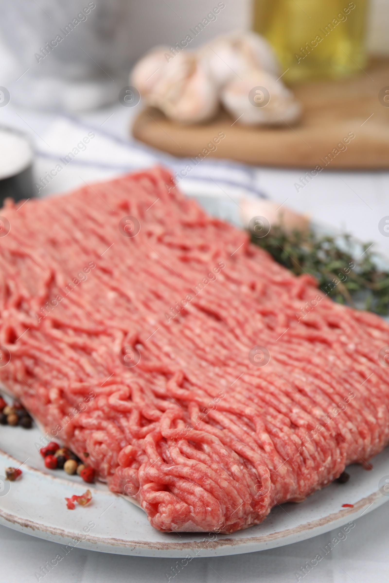 Photo of Fresh raw ground meat and peppercorns on white tiled table, closeup