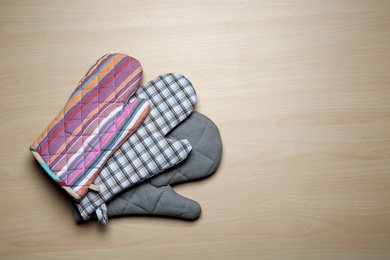 Photo of Three oven gloves on wooden table, flat lay. Space for text