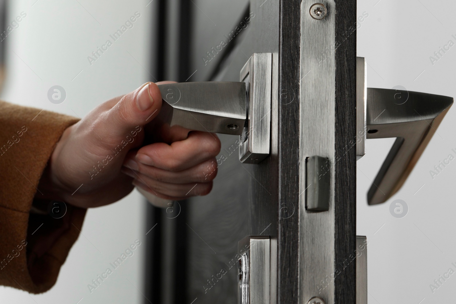 Photo of Woman opening wooden door indoors, closeup of hand on handle