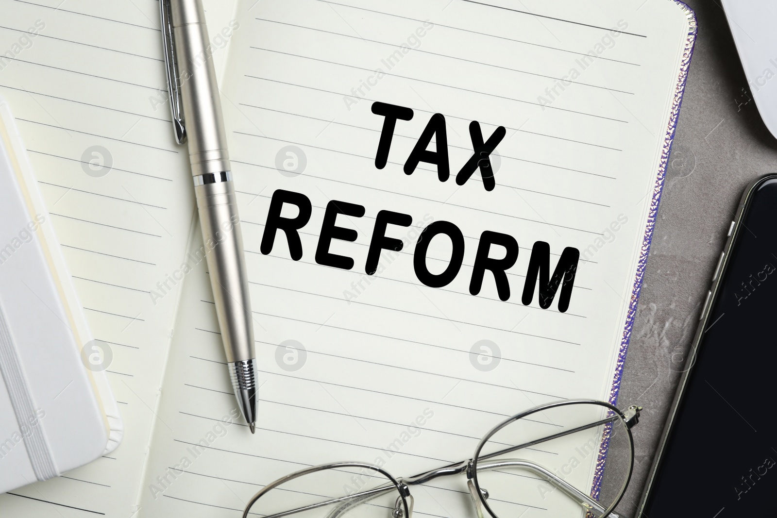 Image of Notebook with words TAX REFORM, pen and glasses on table, closeup