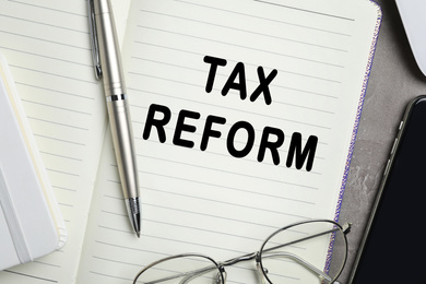Image of Notebook with words TAX REFORM, pen and glasses on table, closeup