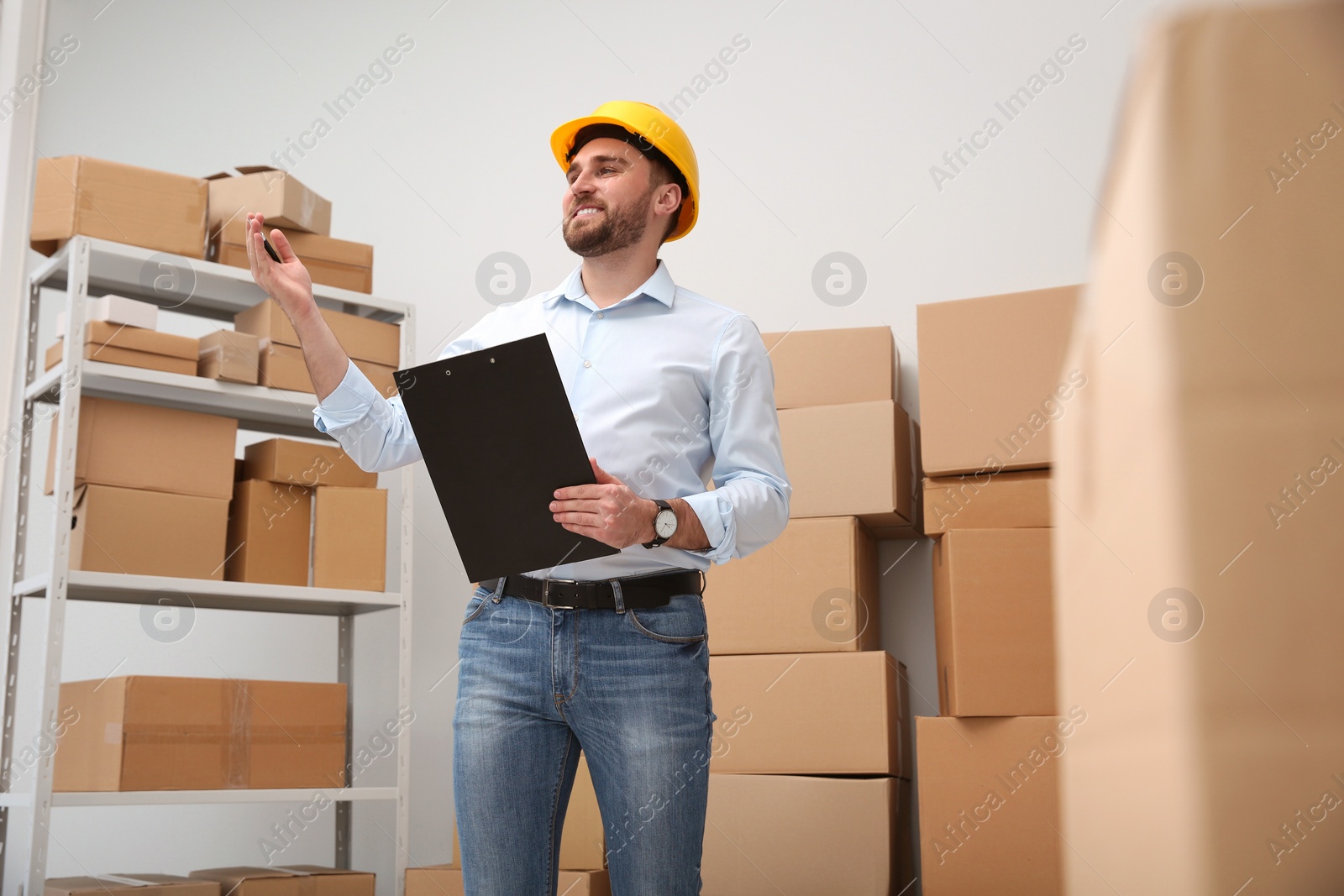 Photo of Young man with clipboard near cardboard boxes at warehouse