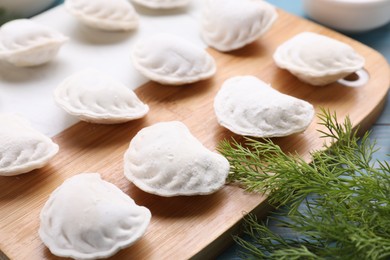 Photo of Raw dumplings (varenyky) and ingredients on light blue table, closeup