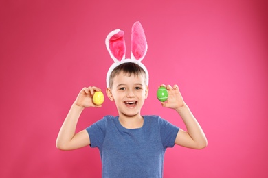 Photo of Little boy in bunny ears headband holding Easter eggs on color background