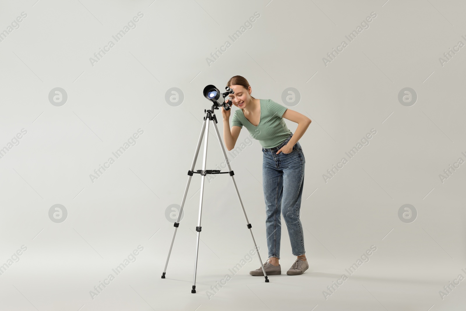 Photo of Young astronomer looking at stars through telescope on grey background