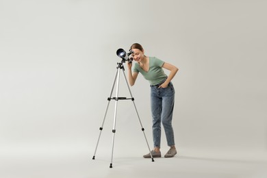 Young astronomer looking at stars through telescope on grey background