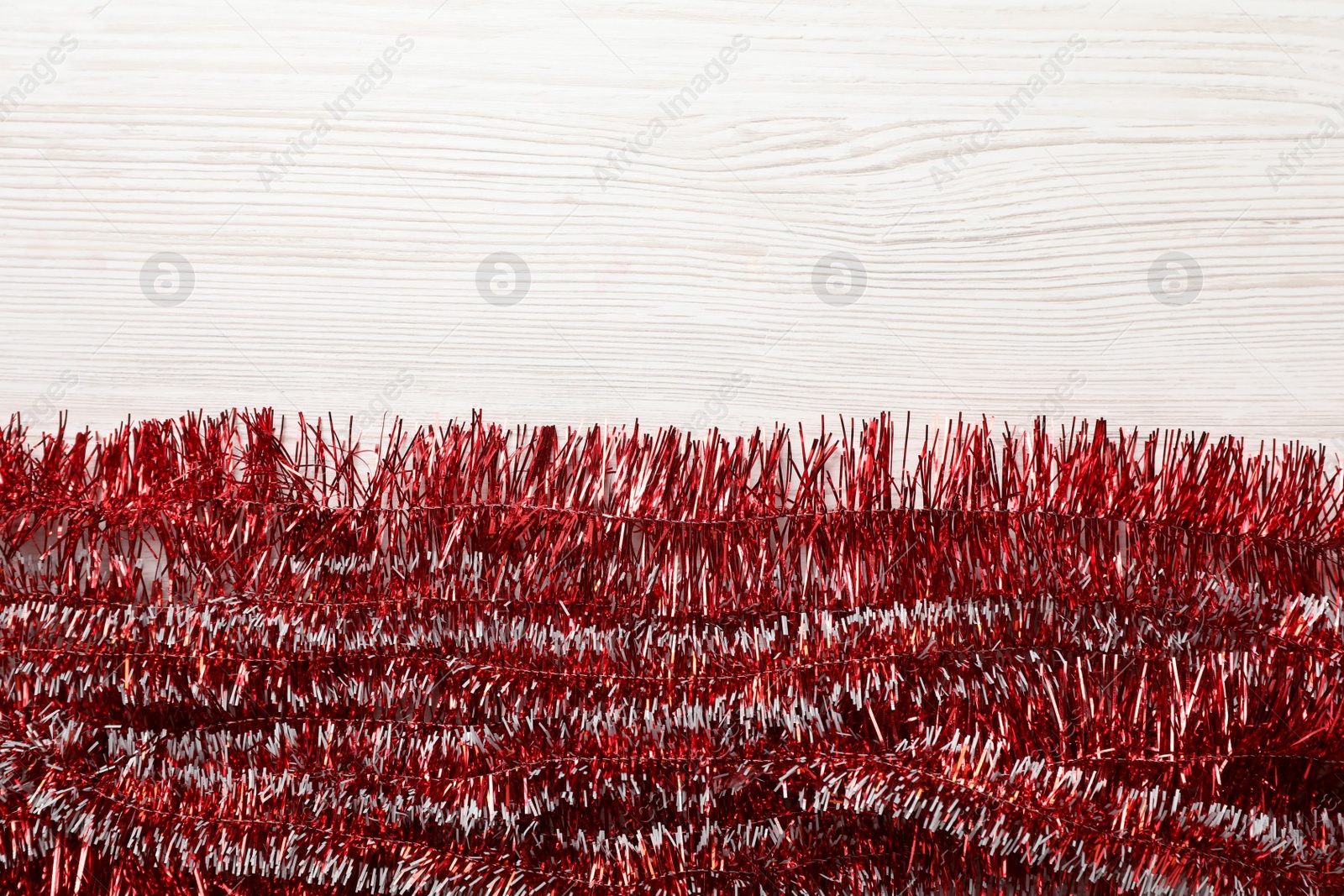 Photo of Shiny red tinsel on white wooden background, flat lay. Space for text