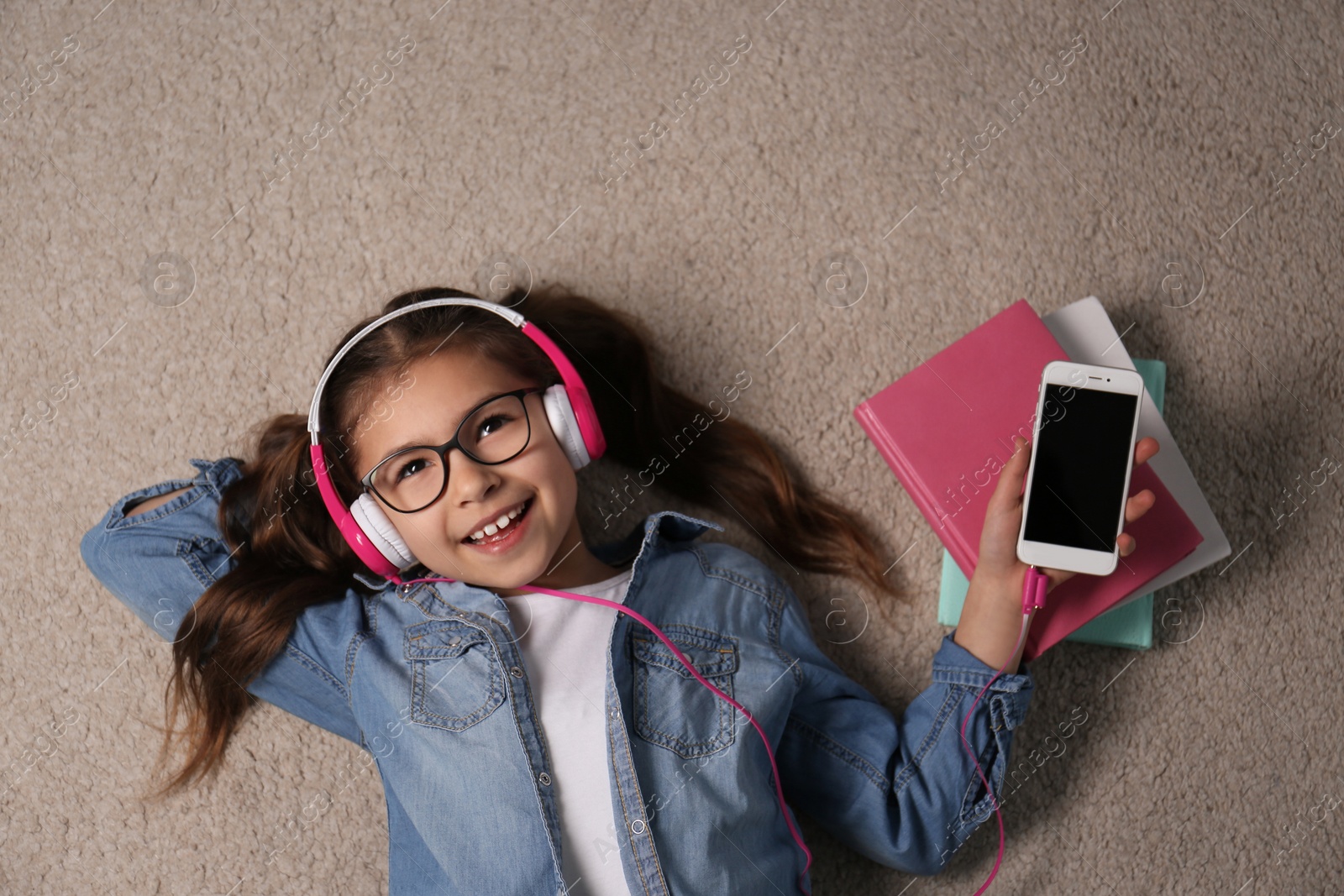 Photo of Cute little girl listening to audiobook on floor, top view