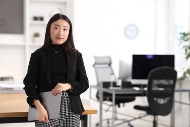 Portrait of beautiful businesswoman with laptop in office. Space for text