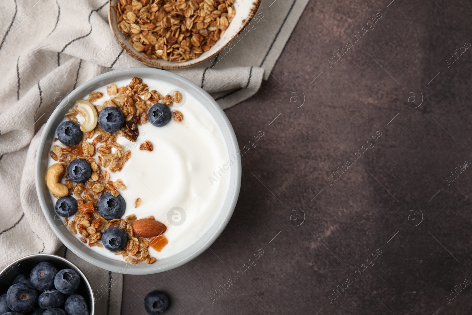 Photo of Bowl with yogurt, blueberries and granola on grey table, top view. Space for text