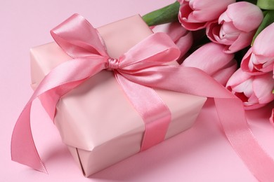 Photo of Beautiful gift box with bow and tulip flowers on pink background, closeup