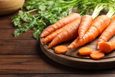 Board with fresh carrots on wooden background, closeup. Space for text