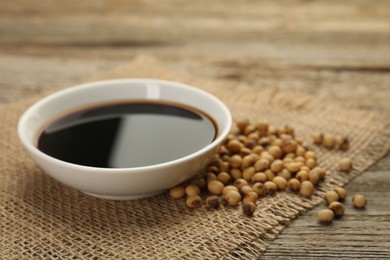 Photo of Soy sauce in bowl and beans on wooden table, closeup. Space for text