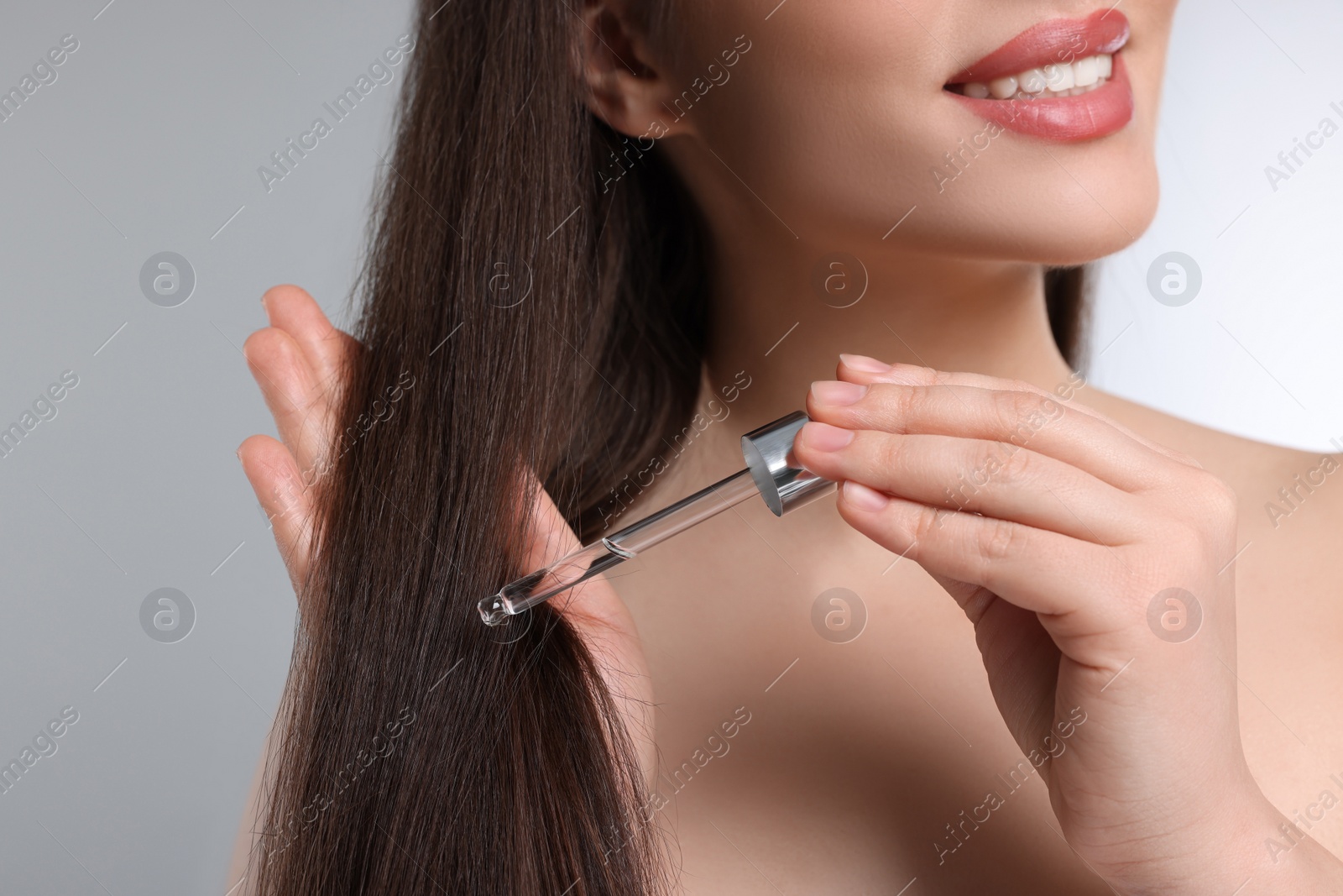 Photo of Happy woman applying essential oil onto hair on light grey background, closeup