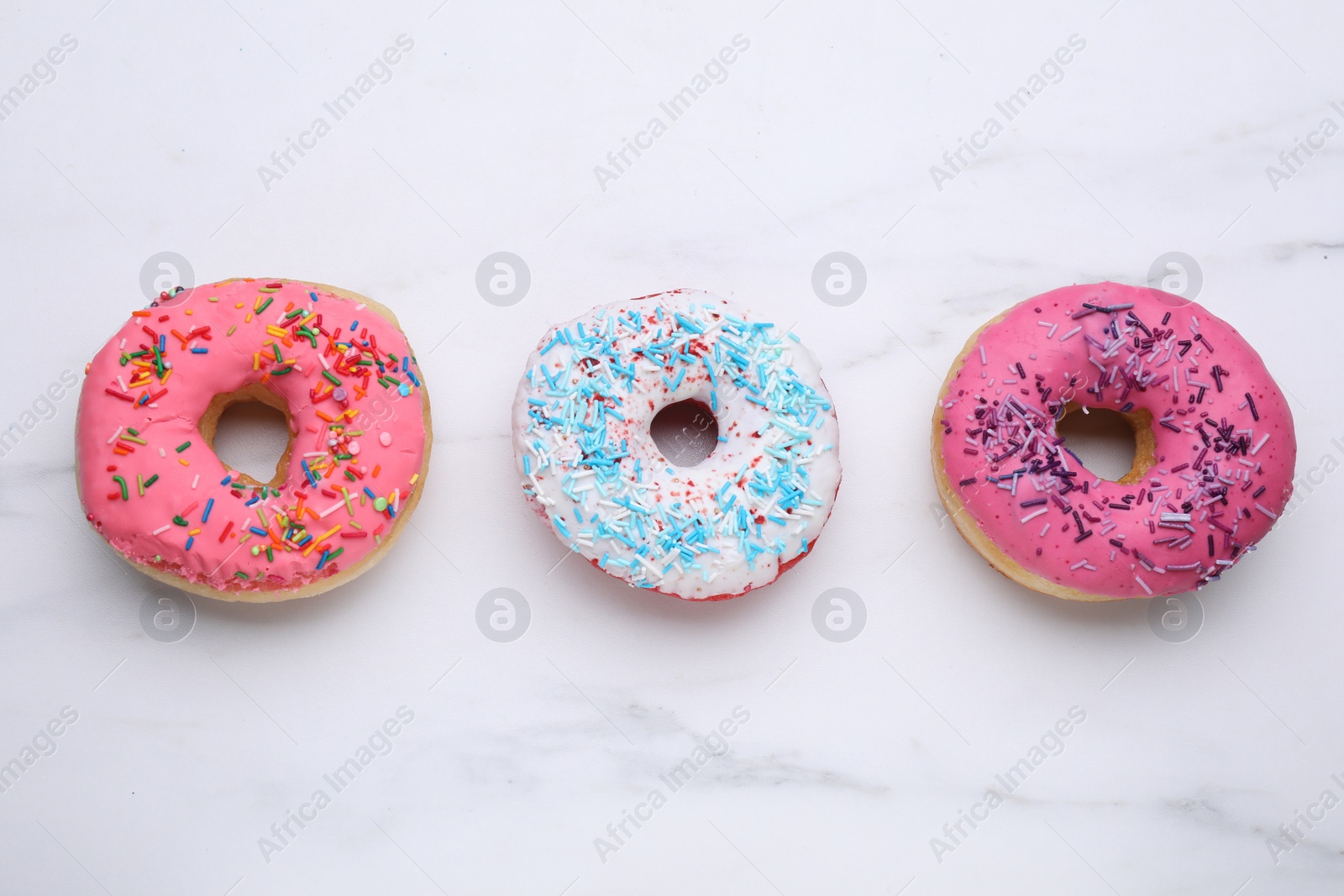 Photo of Sweet glazed donuts decorated with sprinkles on white marble table, flat lay. Tasty confectionery