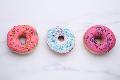 Photo of Sweet glazed donuts decorated with sprinkles on white marble table, flat lay. Tasty confectionery