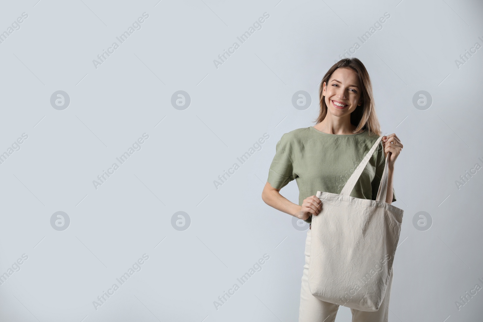 Photo of Happy young woman with blank eco friendly bag on light background. Space for text