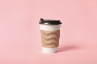Takeaway paper coffee cup with cardboard sleeve on pink background