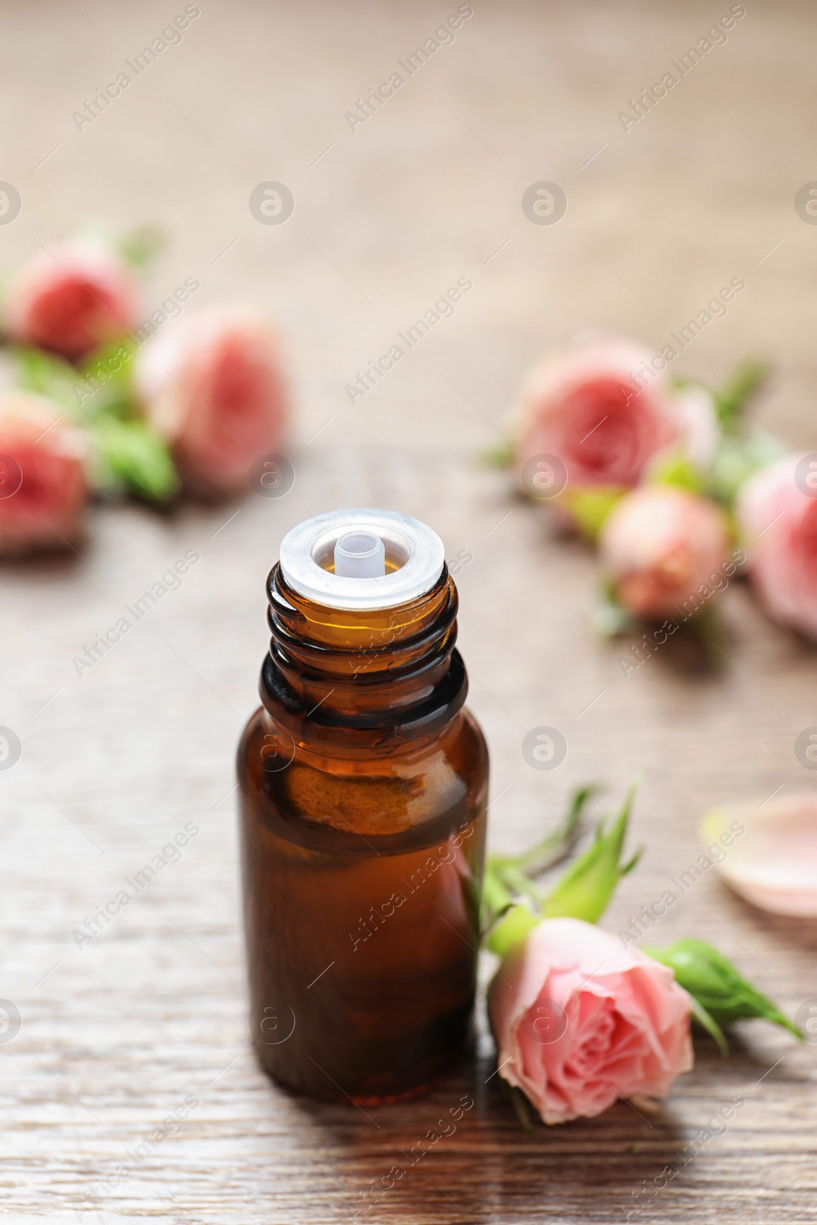 Photo of Bottle of rose essential oil and fresh flowers on wooden table, space for text