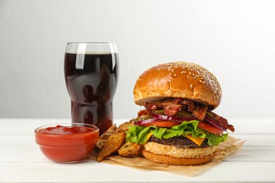 Tasty burger, potato wedges, sauce and refreshing drink on white wooden table. Fast food
