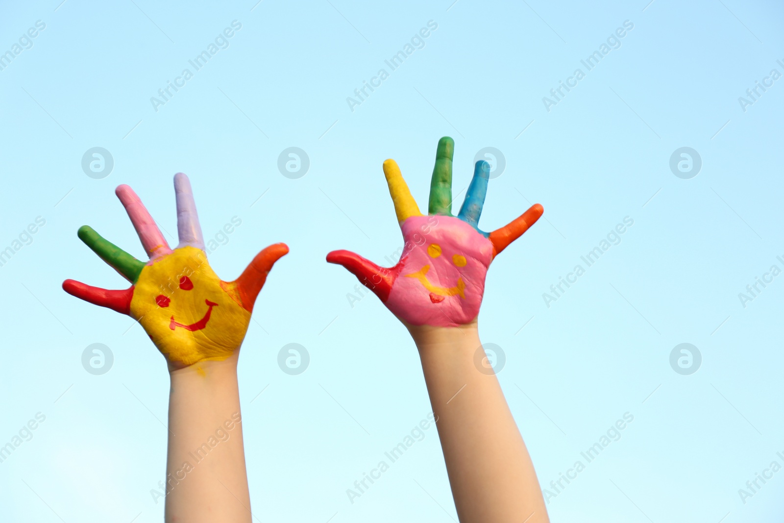 Photo of Kid with smiling face drawn on palms against blue sky, closeup. School holidays