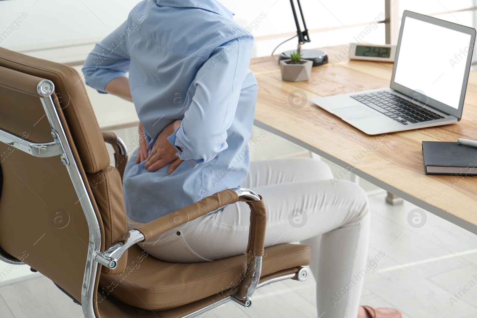 Photo of Woman suffering from back pain at workplace in office, closeup