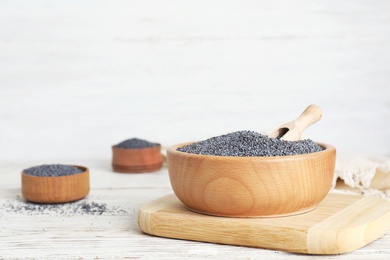 Photo of Poppy seeds in wooden dishware on table. Space for text