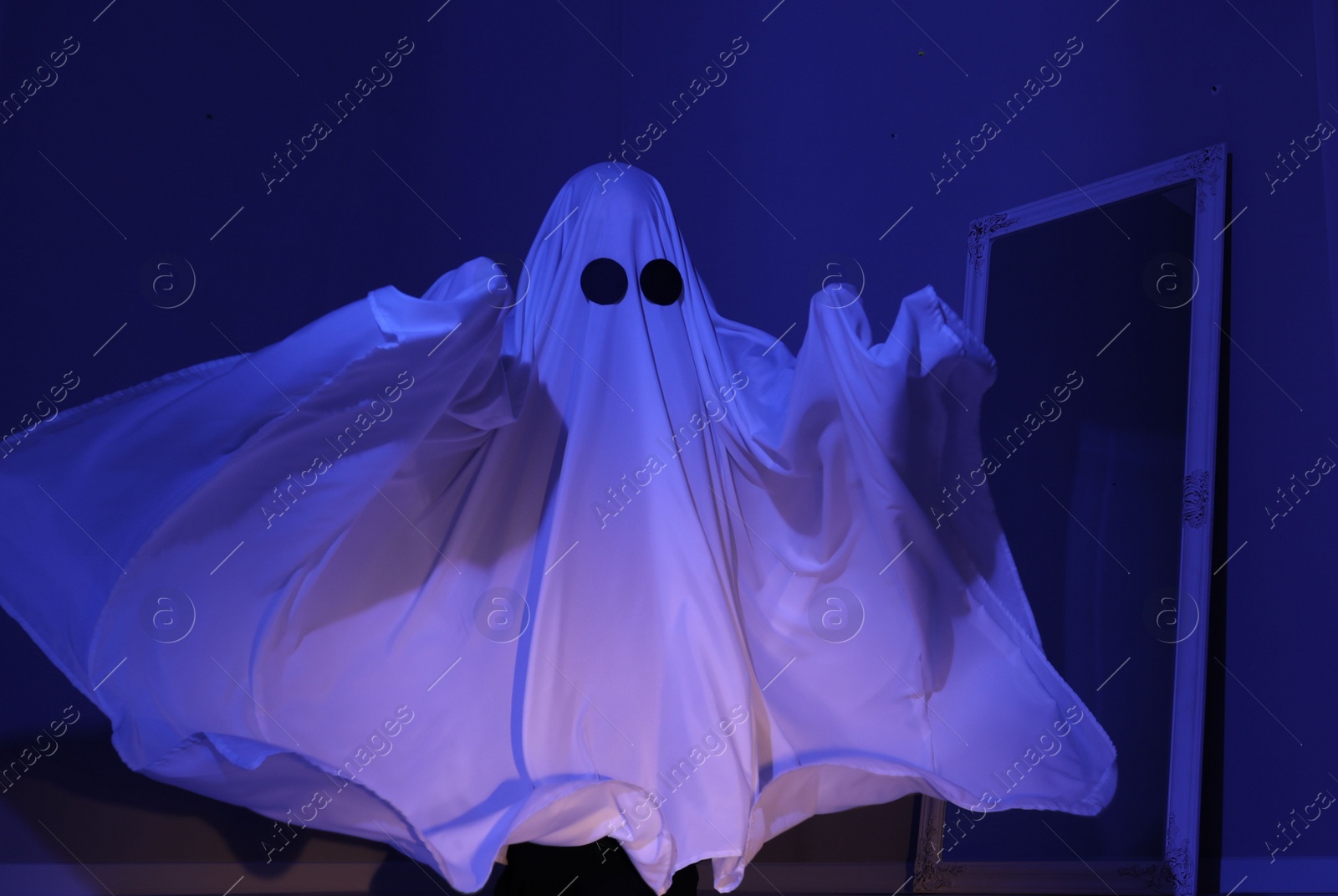 Photo of Creepy ghost. Woman covered with sheet in blue light