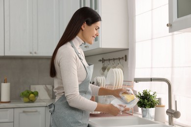 Photo of Happy woman washing bowl at sink in kitchen
