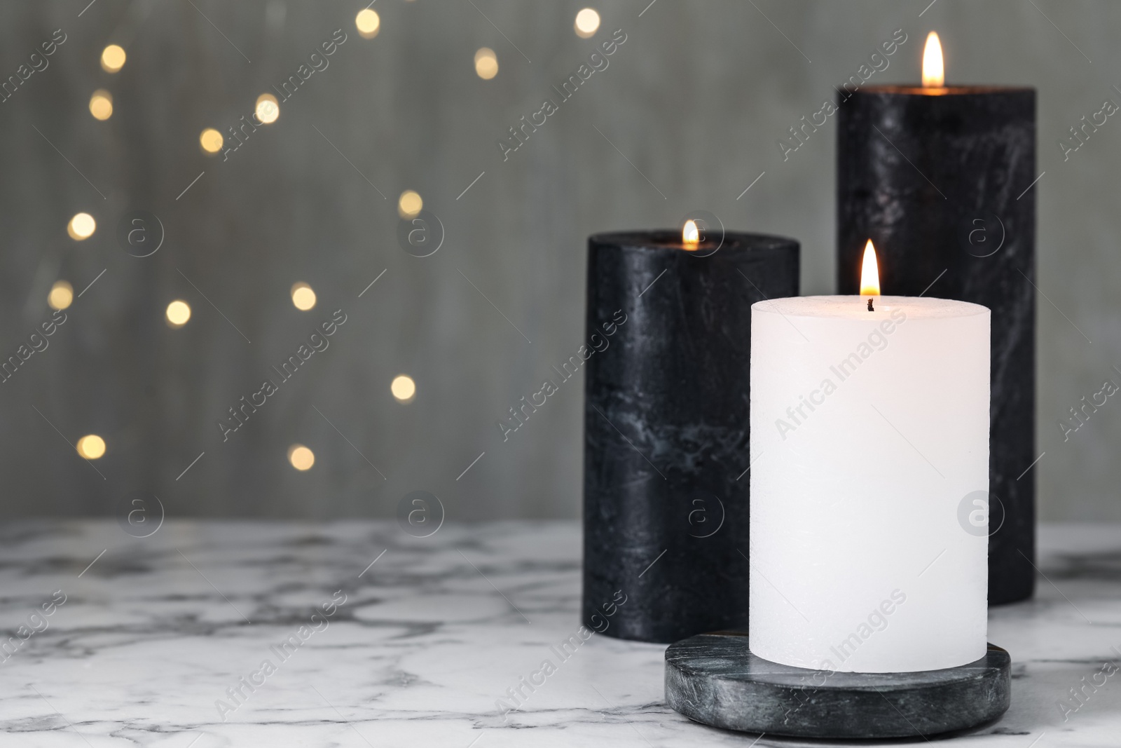 Photo of Burning candles on white marble table against blurred lights, space for text